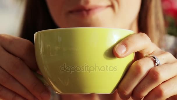 Joven mujer bonita se sienta con una taza de té o café y tragando, de cerca . — Vídeos de Stock
