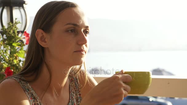 Unga vackra kvinnan sitter på ett café som skådar vacker utsikt över havet bay. — Stockvideo