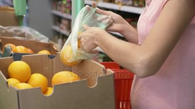 Genç kadın süpermarkette kutusundan bir portakal toplama