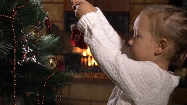 Söt liten tjej dekorera julgran i mörkt rum med öppen spis — Stockvideo