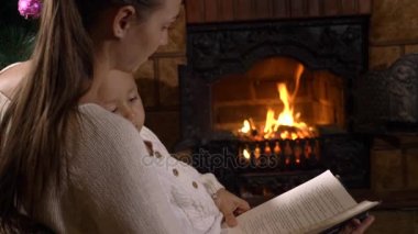 Şömine ve Noel ağacı yanında küçük kızı okuma kitabı ile anne