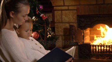 Şömine ve Noel ağacı yanında küçük kızı okuma kitabı ile anne