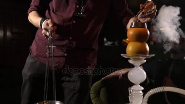Erkekler ise nargile kömürleri değişen genç hookahman sigara içiyor