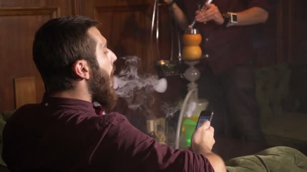 Jonge hookahman veranderen de kolen in de waterpijp terwijl mannen is roken — Stockvideo