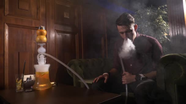 Hezký mladý muž kouří vodní dýmky a dělá kroužky kouře. — Stock video