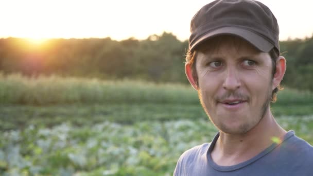 Agricultor parado en el campo de la granja orgánica, comiendo pepino maduro fresco y sonriendo — Vídeos de Stock