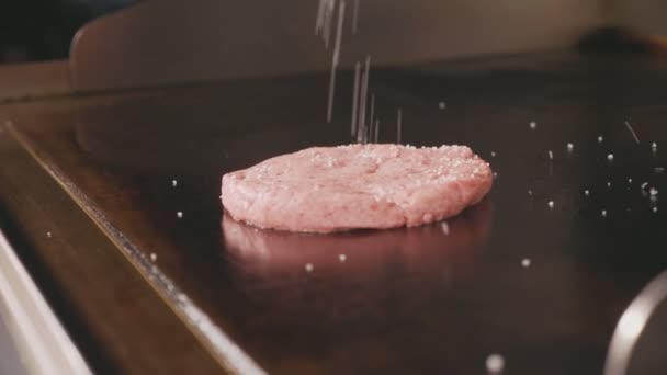 Шеф-повар льет соль на сырую котлету для жарки бургеров на электрическом коммерческом гриле — стоковое видео