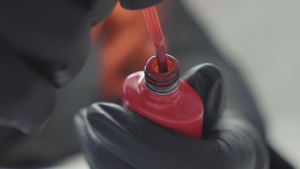 Esmalte de uñas rojo en las manos con guantes negros. Cepillo dentro y fuera de la botella — Vídeo de stock