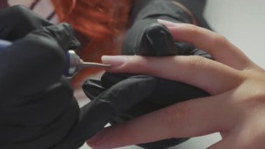 Manikürcü kadın parmaklarına manikür yapmak için elektrikli tırnak matkabı uyguluyor..