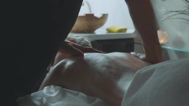 Joven hermosa mujer se encuentra en el sofá en el spa y disfruta de masaje de espalda — Vídeos de Stock
