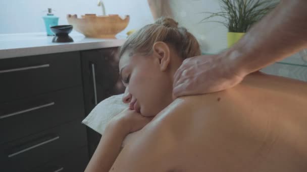 Hermosa chica rubia tumbada en el sofá recibiendo masaje de espalda en el salón de spa de lujo — Vídeo de stock