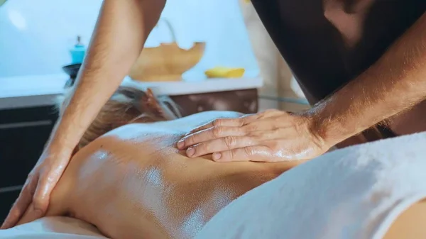 Beautiful blond girl lying on couch receiving back massage at luxury spa salon — Stock Photo, Image