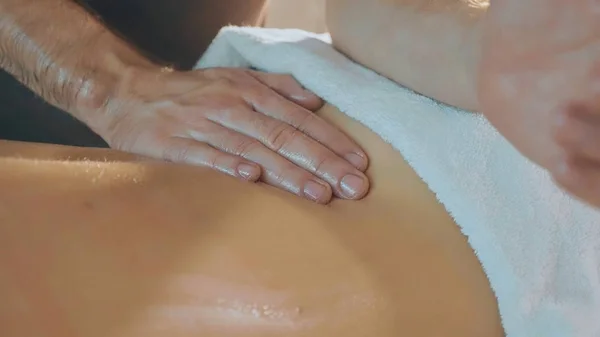 Young beautiful woman lies on couch in spa and enjoys back massage, close-up — Stock Photo, Image