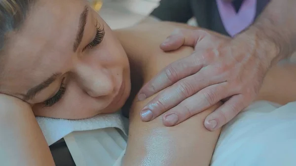 Portrait of blond girl lying on couch receiving back massage at luxury spa salon — Stock Photo, Image