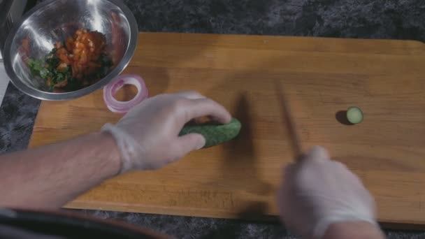 Επαγγελματίας σεφ στο γάντια σε φέτες αγγούρι στο ξύλο του σκάφους σε εμπορική κουζίνα — Αρχείο Βίντεο