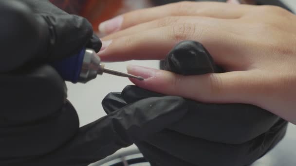マニキュリストは、女性の指にマニキュアに電気ネイルファイルドリルを適用しています. — ストック動画