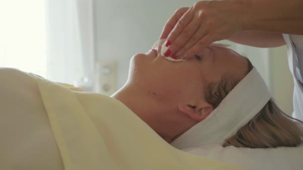 Kosmetolog jest czyszczenie womans twarz gąbką bawełny w salonie spa — Wideo stockowe