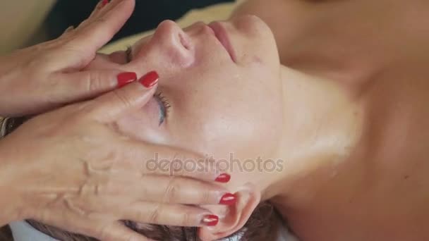 Hermosa joven que se relaja con masaje facial en el salón de spa de lujo, primer plano . — Vídeo de stock