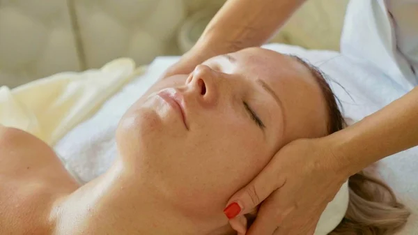 Belle jeune femme relaxante avec massage du visage au salon de spa de luxe, gros plan . — Photo