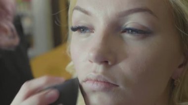 Modelleri yüzünde kapatıcı uygulayarak genç makyaj sanatçısı.