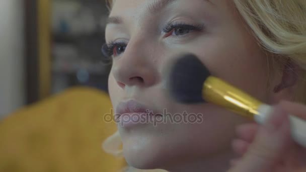 Молодой визажист наносит маскировку на лицо модели . — стоковое видео
