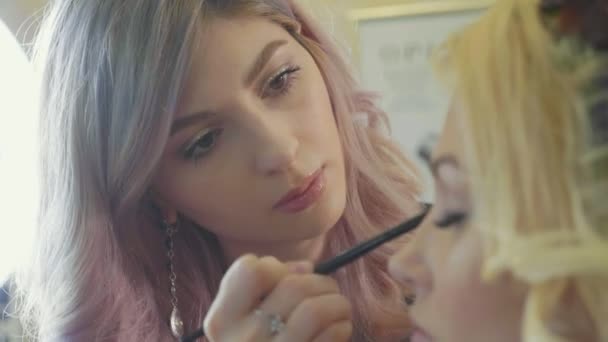 Jeune maquilleuse appliquant des cosmétiques sur les yeux des mannequins . — Video