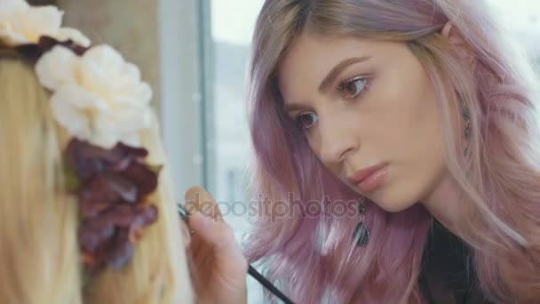 Young makeup artist applying cosmetics on models eyes. — Stock Video