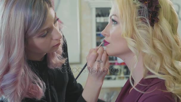 Young makeup artist applying lipstick on models lips. — Stock Video
