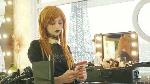 Krásná mladá dívka s makeupem halloween pomocí chytrého telefonu v beauty salonu — Stock video