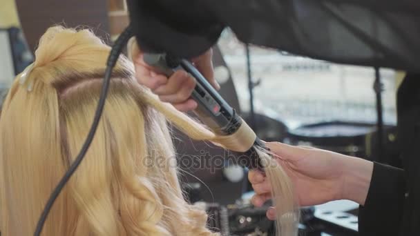 Женщина парикмахер делает кудри на светлые волосы с щипцами для завивки в салоне красоты . — стоковое видео