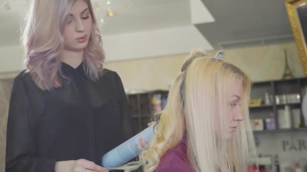 Parrucchiere di donna che fa riccioli a capelli biondi con ferri da stiro ricci a salone di bellezza . — Video Stock