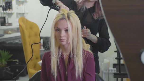 Vrouw kapper maken krullen bij blond haar met krultangen bij beauty salon. — Stockvideo