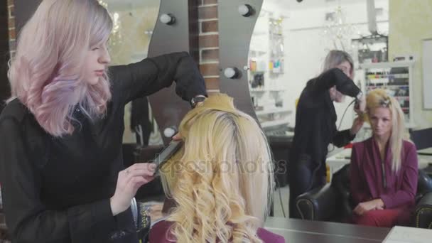 Peluquería mujer haciendo rizos en el pelo rubio con rizadores en el salón de belleza . — Vídeo de stock