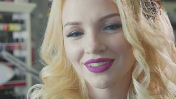 Красивая блондинка с длинными вьющимися волосами и макияжем, позирующая перед камерой — стоковое видео