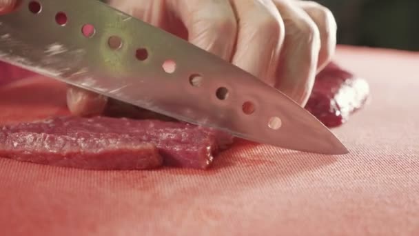 El chef corta carne cruda con el cuchillo en pizarra roja, primer plano cámara lenta — Vídeo de stock