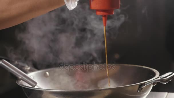 Gros plan du chef verse la sauce dans les aliments frits dans une poêle à wok, au ralenti . — Video