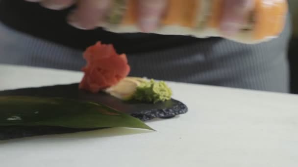 Close-up van sushi chef-kok in handschoenen zet de broodjes op ingerichte plaat. — Stockvideo