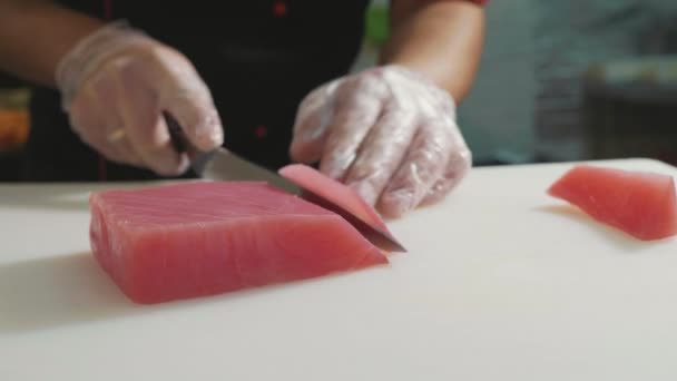 Nahaufnahme eines Sushi-Kochs in Handschuhen schneidet frisches rotes Fischfilet an der Sushi-Bar. — Stockvideo