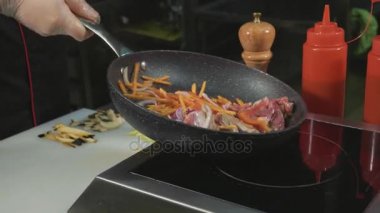 Şef çeşitli sebze ve et üzerine sıcak bir tavada tereyağı ile patates kızartması