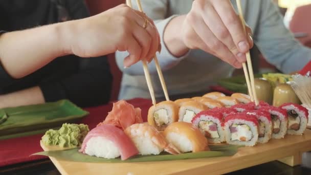 Young couple with chopsticks takes sushi from a plate in a japanese restaurant. — Stock Video
