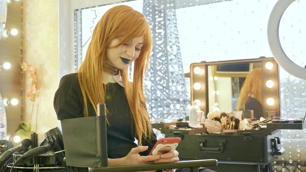 Menina bonita nova com maquiagem halloween usando telefone inteligente no salão de beleza — Fotografia de Stock
