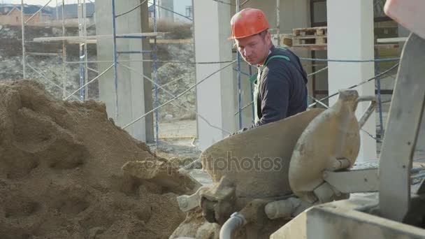 Kaukasiska arbetare häller sand i en betongblandare med spade på byggarbetsplats — Stockvideo