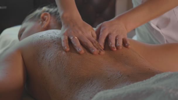 Spa therapist applying scrub on young woman back at luxury beauty salon. — Stock Video