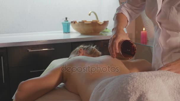 Spa therapist pouring hot chocolate on young woman back at luxury beauty salon — Stock Video