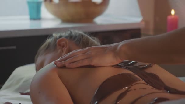 Esteticista haciendo masaje con chocolate a joven hermosa mujer en el salón de spa — Vídeos de Stock