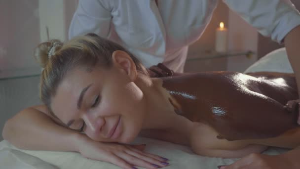 Beautician doing massage with chocolate to young beautiful woman at spa salon — Stock Video