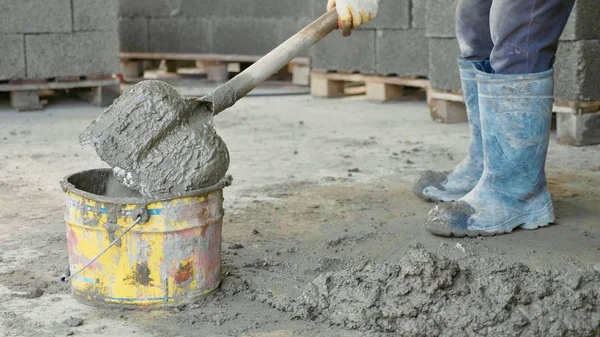 Worker shoveling mixing a concrete and puts it in bucket at construction site.