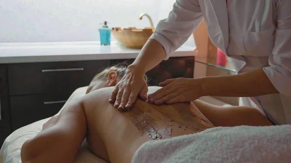Spa therapist applying scrub on young woman back at luxury beauty salon. — Stock Photo, Image