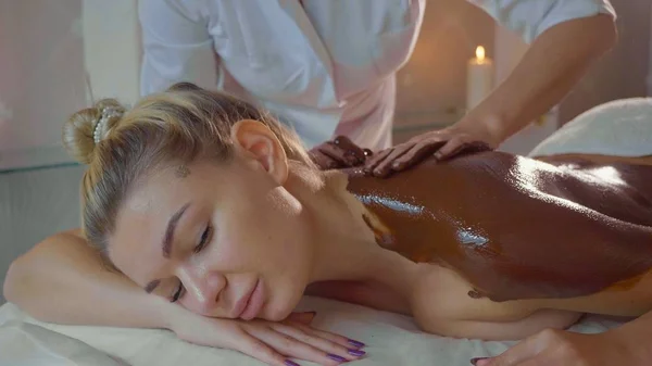 Esthéticienne faisant massage avec du chocolat à jeune belle femme au salon de spa — Photo