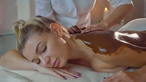 Kosmetolog gör massage med choklad till unga vackra kvinnan på spasalong — Stockfoto